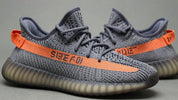 Noul Yeezy Beluga, pantofi sport gri cu dungă portocalie.